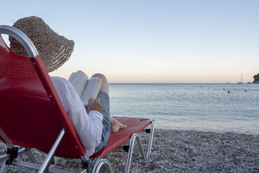 Greece, Parga, woman on deckchair reading book on the beach at sunset - PSIF00092