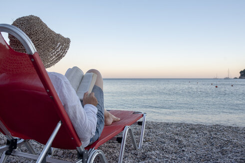 Griechenland, Parga, Frau auf Liegestuhl liest Buch am Strand bei Sonnenuntergang - PSIF00092