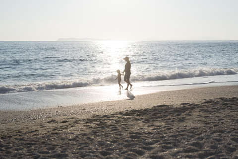 Griechenland, Parga, Mutter und Tochter spazieren am Strand bei Sonnenuntergang, lizenzfreies Stockfoto