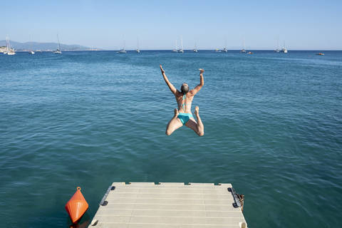 Griechenland, Parga, unbekümmerte Frau springt vom Steg ins Meer, lizenzfreies Stockfoto