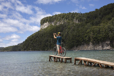 Fahrradfahrer macht Foto auf kleinem Steg am Bergsee - AURF06002