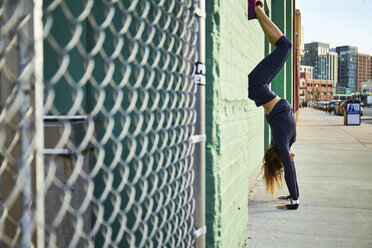 Frau macht Handstand auf dem Gehweg neben einem Maschendrahtzaun, Boston, Massachusetts, USA - AURF06083