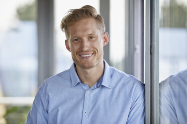 Portrait of smiling young man leaning against window - RBF06792