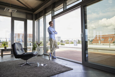 Young man standing at balcony door looking out - RBF06805