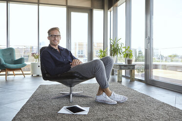 Portrait of smiling young man sitting in armchair at the window at home - RBF06811