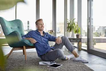 Lächelnder junger Mann sitzt mit Tablet und Notizblöcken zu Hause auf dem Teppich - RBF06818