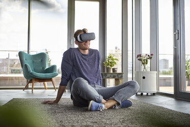 Young man sitting on carpet at home wearing VR glasses - RBF06825