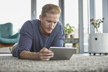 Young man lying on carpet at home using tablet - RBF06827