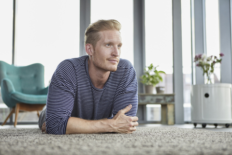 Junger Mann liegt zu Hause auf dem Teppich, lizenzfreies Stockfoto