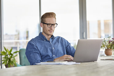 Junger Mann sitzt am Tisch und benutzt einen Laptop - RBF06834