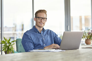 Portrait of smiling young man sitting at table using laptop - RBF06835
