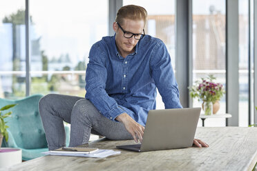 Junger Mann sitzt auf einem Tisch und benutzt einen Laptop - RBF06838