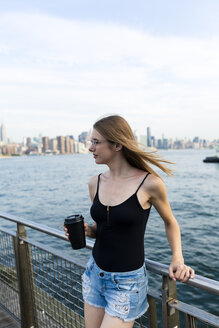 Junge Frau mit Blick über den East River, in der Hand eine Tasse Kaffee - GIOF04506