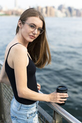 Junge Frau mit Blick über den East River, in der Hand eine Tasse Kaffee - GIOF04507