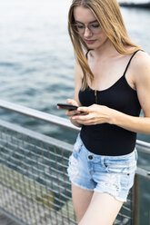 Junge Frau steht am East River und benutzt ein Smartphone - GIOF04508