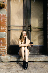 Young woman sitting in the street on a doorstep, holding a cup of coffee - GIOF04526