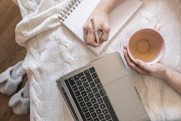 Frau mit Tasse Tee und Laptop bei der Arbeit zu Hause, Teilansicht - FLMF00064