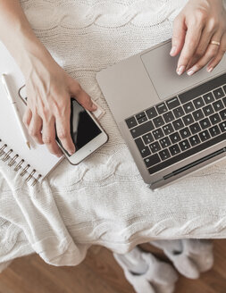 Frau arbeitet auf dem Bett mit Laptop und Smartphone, Teilansicht - FLMF00065