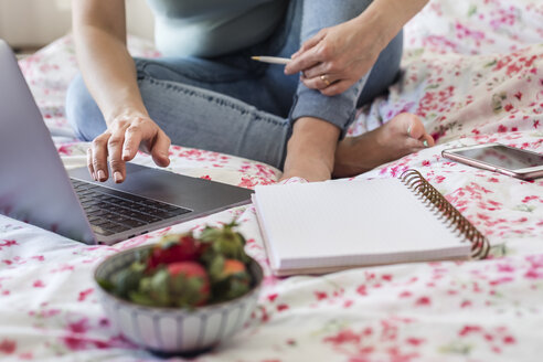 Frau sitzt zu Hause auf dem Bett und arbeitet mit einem Laptop, Teilansicht - FLMF00070