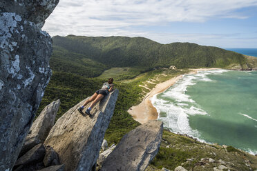 Young woman lying on edge of rock with view from Pico da Coroa Hill to Lagoinha do Leste Beach, Florianopolis, Santa Catarina Island, Brazil - AURF06112