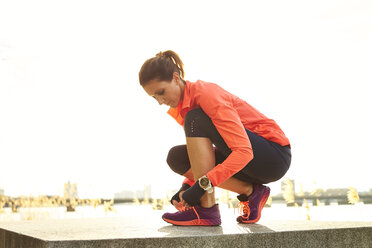 Female jogger tying shoes against clear sky, Boston, Massachusetts, USA - AURF06209