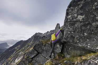 Female hiker climbing steep rocky ridge towards Osthimmeltind mountain peak - AURF06221