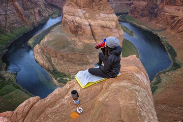 Wanderin trinkt Kaffee auf einer Klippe am Horseshoe Bend des Colorado River, Arizona, USA - AURF06251