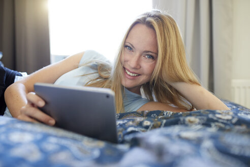 Lachende junge Frau, die zu Hause auf dem Bett liegt und ein digitales Tablet benutzt - PNEF00946