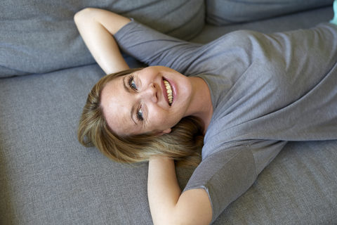 Lachende junge Frau, die sich auf der Couch entspannt, lizenzfreies Stockfoto