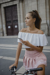 Fashionable young woman exploring Barcelona with a bicycle, using smartphone - AFVF01590