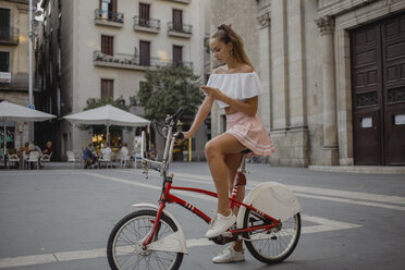 Modische junge Frau, die Barcelona mit dem Fahrrad erkundet und ihr Smartphone benutzt - AFVF01591