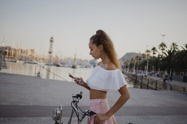 Modische junge Frau, die Barcelona mit dem Fahrrad erkundet und ihr Smartphone benutzt - AFVF01597