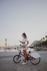 Modische junge Frau, die Barcelona mit dem Fahrrad erkundet und ihr Smartphone benutzt - AFVF01599