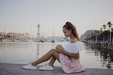 Fashionalble young woman sitting at the harbour of Barcelona, using smartphone - AFVF01608