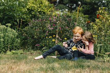 Siblings playing on field against flowering plants at park - CAVF48789