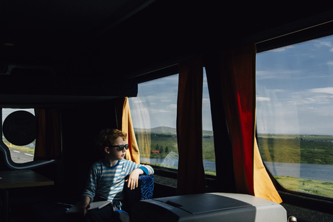 Junge mit Sonnenbrille, der im Wohnmobil sitzend durch das Fenster schaut, lizenzfreies Stockfoto