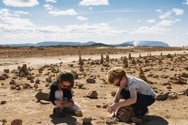 Geschwister spielen mit Steinen in der Wüste an einem sonnigen Tag - CAVF48799