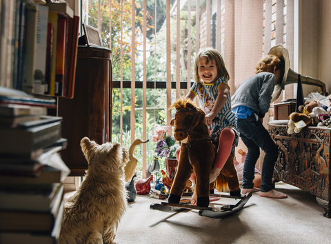 Glückliche Geschwister, die zu Hause spielen, mit einem sitzenden Hund im Vordergrund, lizenzfreies Stockfoto