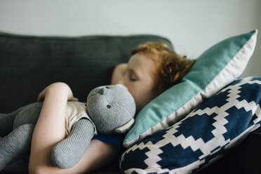 Seitenansicht eines Jungen, der mit einem Teddybär auf der Couch schläft, zu Hause - CAVF48811