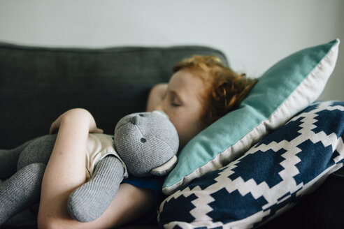 Seitenansicht eines Jungen, der mit einem Teddybär auf der Couch schläft, zu Hause - CAVF48811
