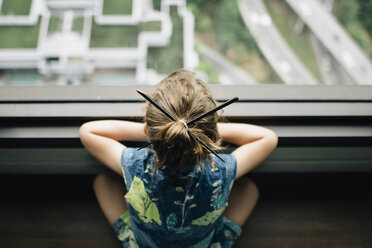 Hoher Blickwinkel eines Mädchens mit japanischen Haarnadeln, das durch das Fenster schaut, während es zu Hause sitzt - CAVF48812