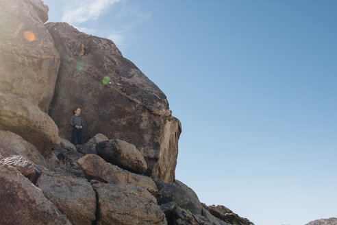 Low angle view of boy standing on rocks against sky during summer - CAVF48815