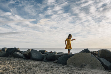 Playful Mädchen zu Fuß auf Felsen am Strand gegen bewölkten Himmel bei Sonnenuntergang - CAVF48816