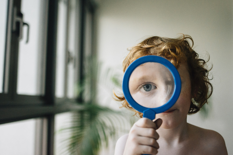 Portrait of shirtless boy playing with magnifying glass at home stock photo