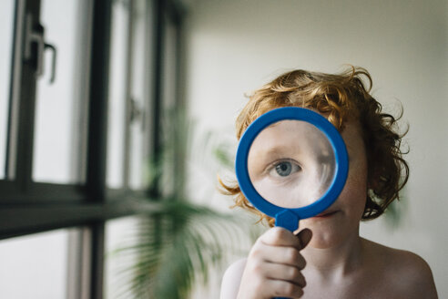 Porträt eines Jungen ohne Hemd, der zu Hause mit einem Vergrößerungsglas spielt - CAVF48818