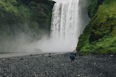 Geschwister stehen vor einem plätschernden Wasserfall im Wald, lizenzfreies Stockfoto