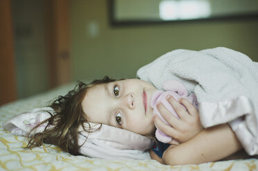 Porträt eines Mädchens mit Stofftier, das zu Hause auf dem Bett liegt - CAVF48825
