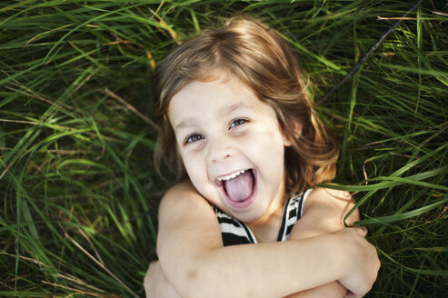 Hochwinkliges Porträt eines glücklichen Mädchens, das auf einer Wiese im Park liegt - CAVF48826