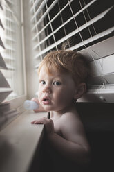 Portrait of shirtless baby boy standing by window at home - CAVF48830