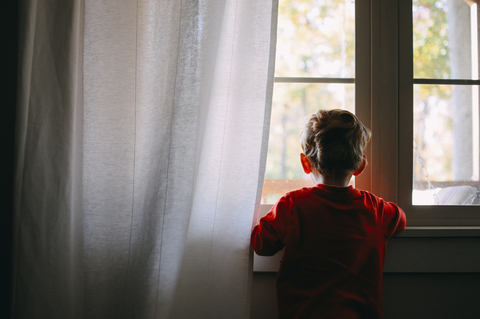 Rückansicht eines kleinen Jungen, der durch ein Fenster zu Hause schaut, lizenzfreies Stockfoto